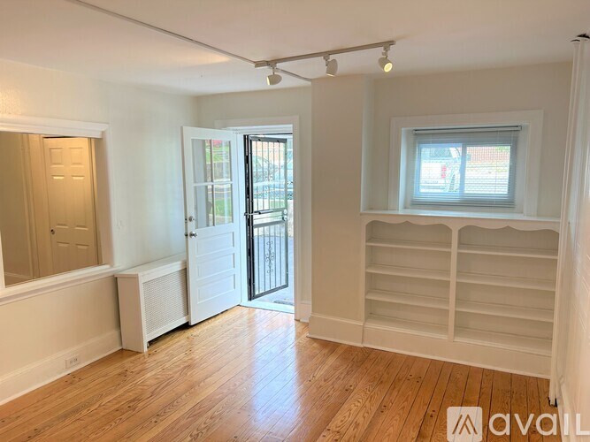 A room with wooden floors and white walls, a window with white blinds, and a sliding glass door leading outside.