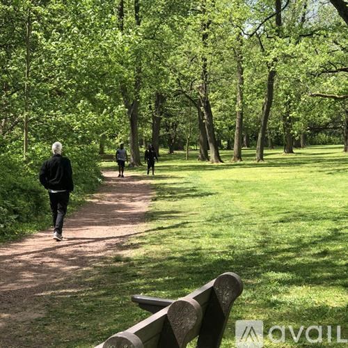 A park with people walking on a path and a bench on the side.