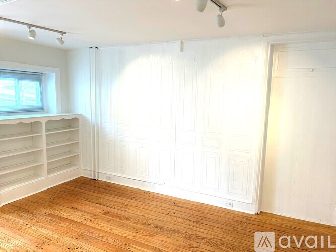 A room with wooden floors and white walls, with a window on the left side.