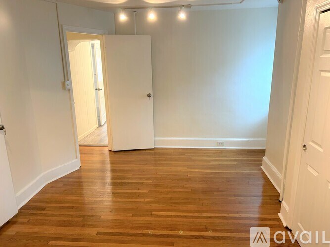 A room with wooden floors and white walls, with a door on the left and a wall on the right.