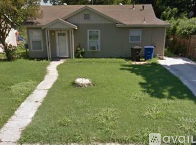 A house with a green lawn and a blue trash bin.