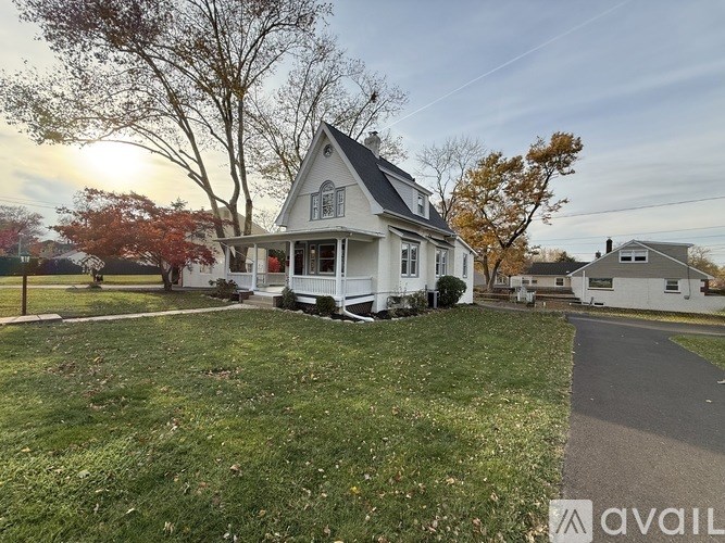 A house with a white exterior and a grey roof is surrounded by a grassy lawn and trees.