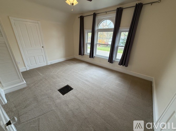 A room with a carpeted floor, a window with black curtains, and a white door.