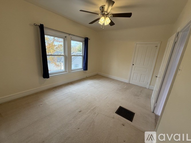 A room with a ceiling fan and a window with black curtains.