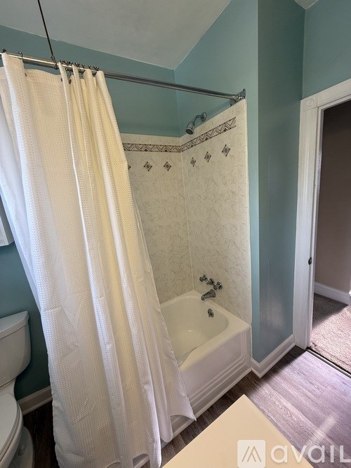 A white shower curtain hangs over a white bathtub in a bathroom.