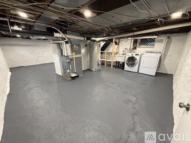 A large, empty basement with concrete floors and walls, and a washing machine and dryer in the corner.
