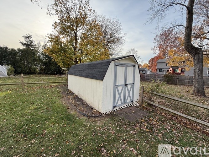 A small white shed with a black roof is situated in a grassy area.