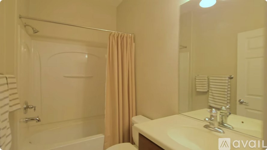 A bathroom with a white tub and sink, a beige shower curtain, and a mirror.