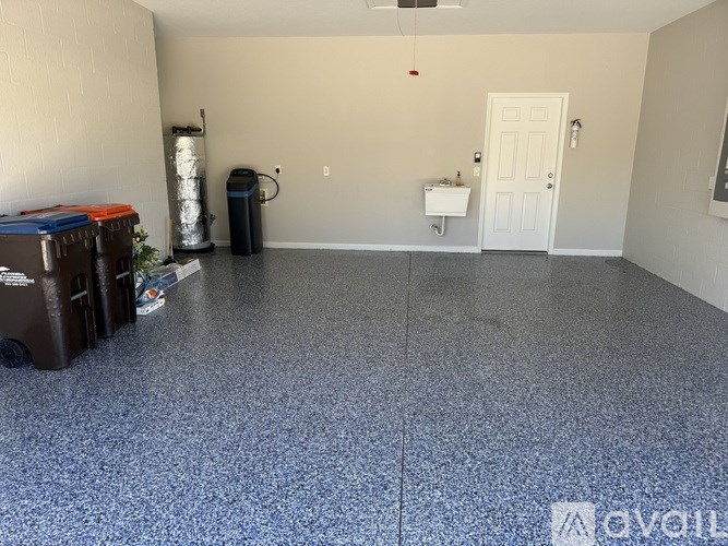 A room with a white door, a trash can, and a floor with a speckled pattern.