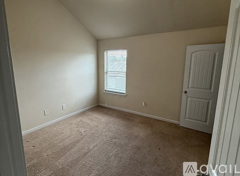 A room with a carpeted floor, a window with blinds, and a white door.