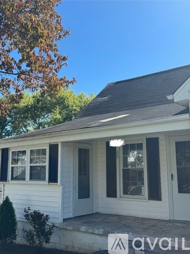 A house with a white exterior and a grey roof with a tree in the background.
