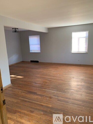 A room with wooden flooring and two windows.