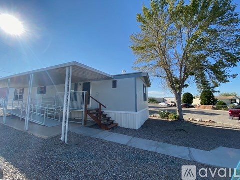 A mobile home with a gravel driveway and a tree in the background.