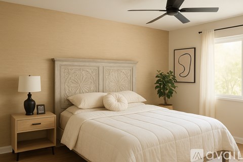 A bedroom with a large bed, a ceiling fan, and a nightstand with a lamp.