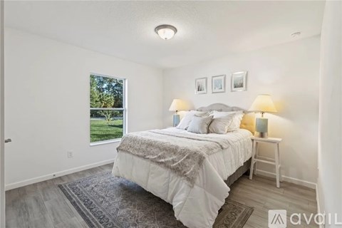 A bedroom with a large bed and a window overlooking a green lawn.