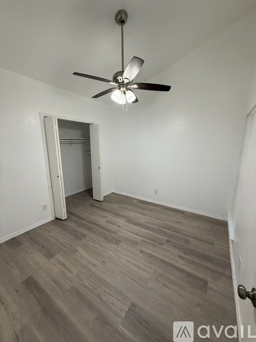 A room with a ceiling fan and light fixture, a door, and a wooden floor.