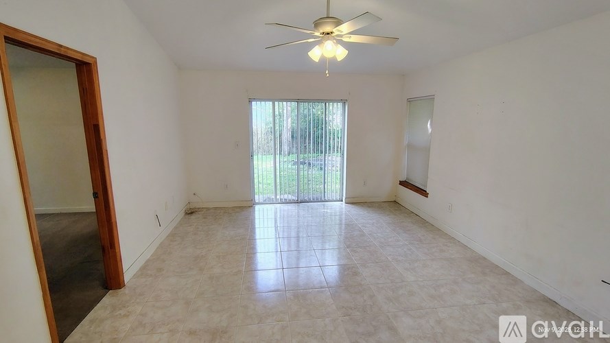 A spacious room with a ceiling fan and a sliding glass door leading to a balcony.