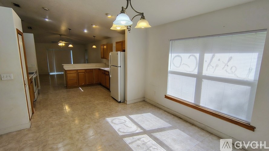 A kitchen with a refrigerator, cabinets, and a window with blinds.
