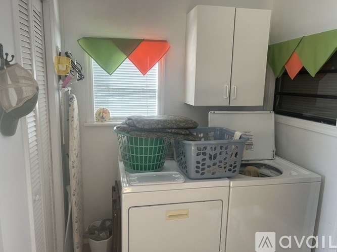 A laundry room with a washer and dryer, a basket on top of the dryer, and a window with a green and red triangle shade.