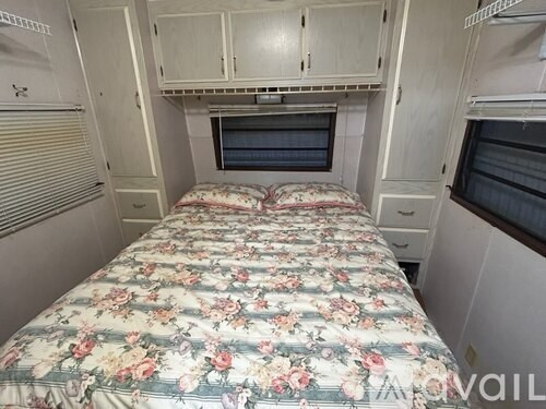 A bed with a floral patterned bedspread sits in a small room with a window and a cabinet above it.