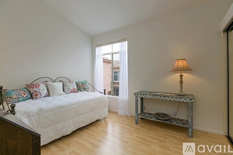 A bedroom with a bed, a table with a lamp, and a window with curtains.