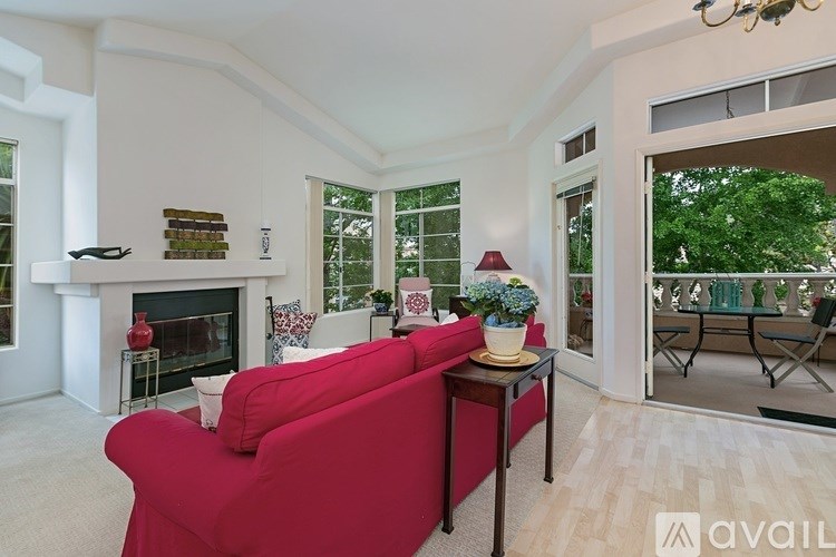 A red couch sits in a living room with a fireplace and a chandelier.