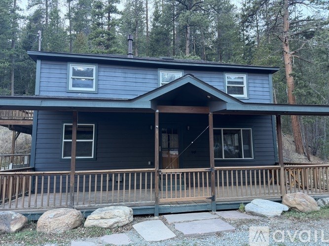 A house with a porch and a balcony is surrounded by rocks and trees.
