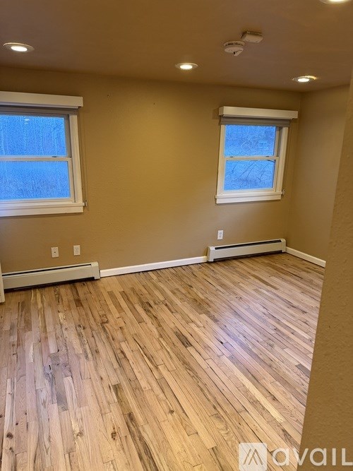 A room with wooden flooring and two windows.