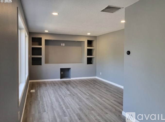 A spacious room with wooden flooring and built-in shelves.