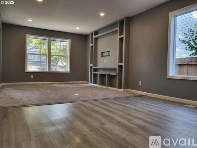 A spacious room with wood flooring and a large window.
