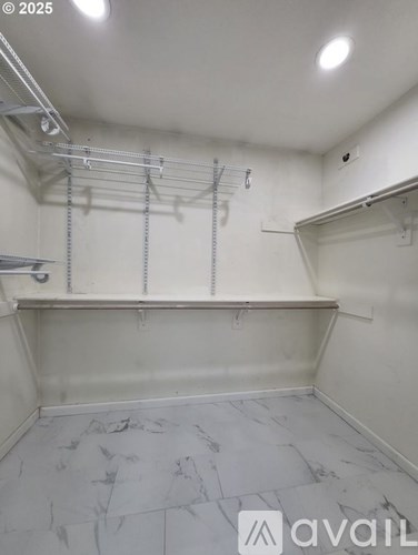A room with a marble floor and white walls, with a shelf and a rack of clothes hangers.