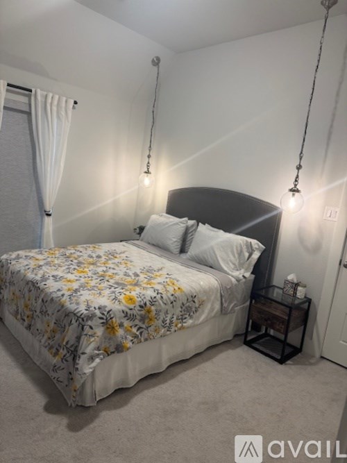 A bed with a floral comforter and two pillows sits in a room with a hanging light fixture.