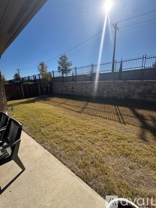 A sunny day in a backyard with a fence and a chair.