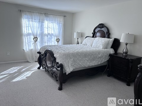 A bedroom with a large bed and a window with curtains.