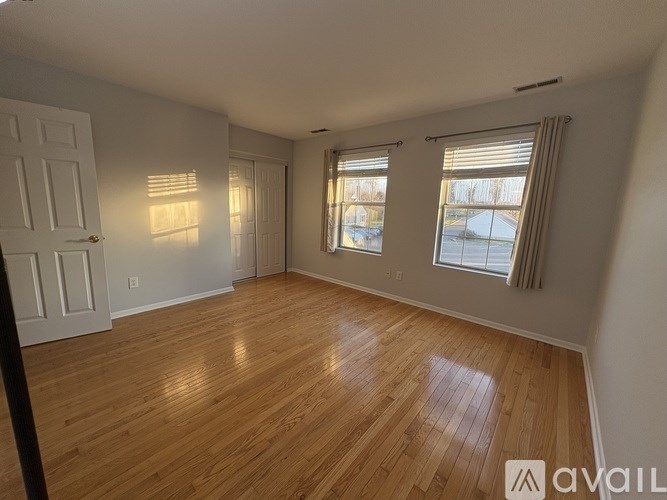 A room with wooden flooring and two windows.