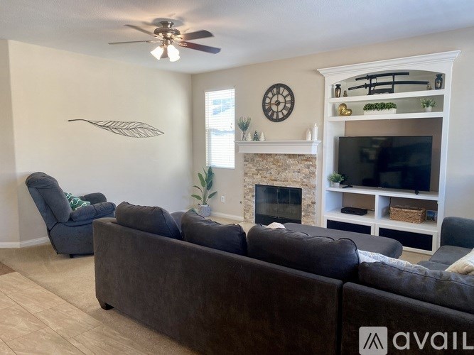 A living room with a grey couch, a fireplace, and a ceiling fan.