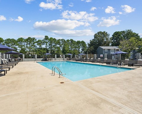 A large swimming pool surrounded by trees and a building in the background.
