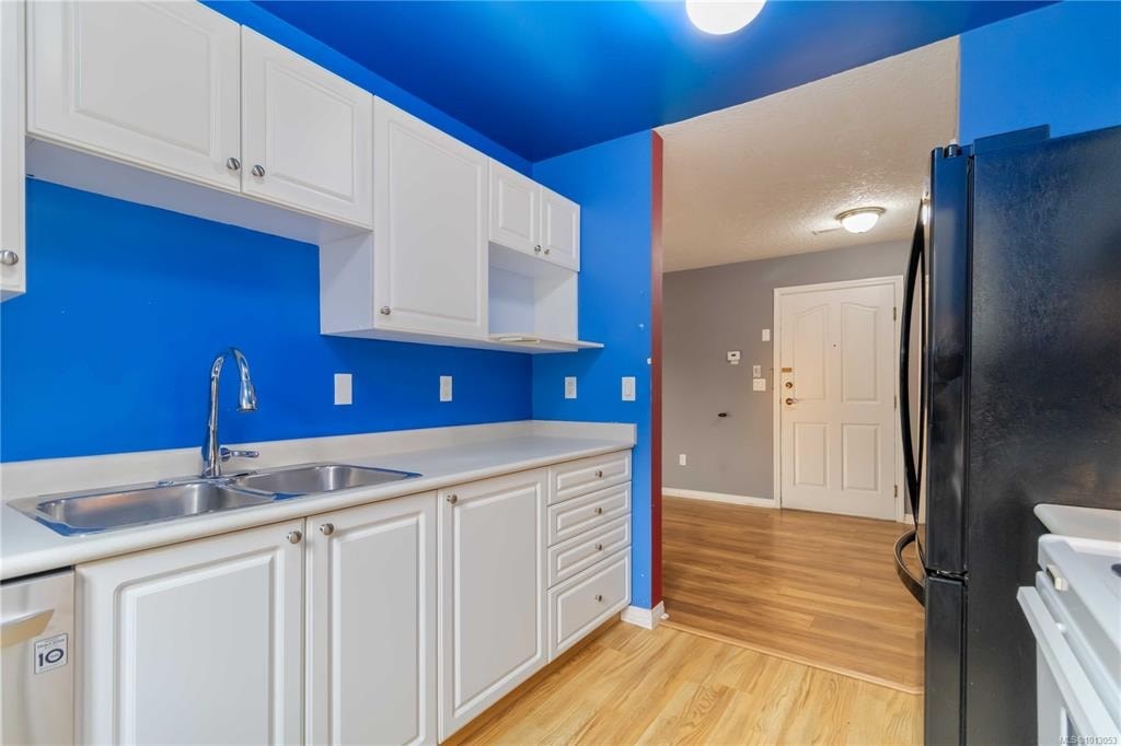 A kitchen with white cabinets and a black refrigerator.