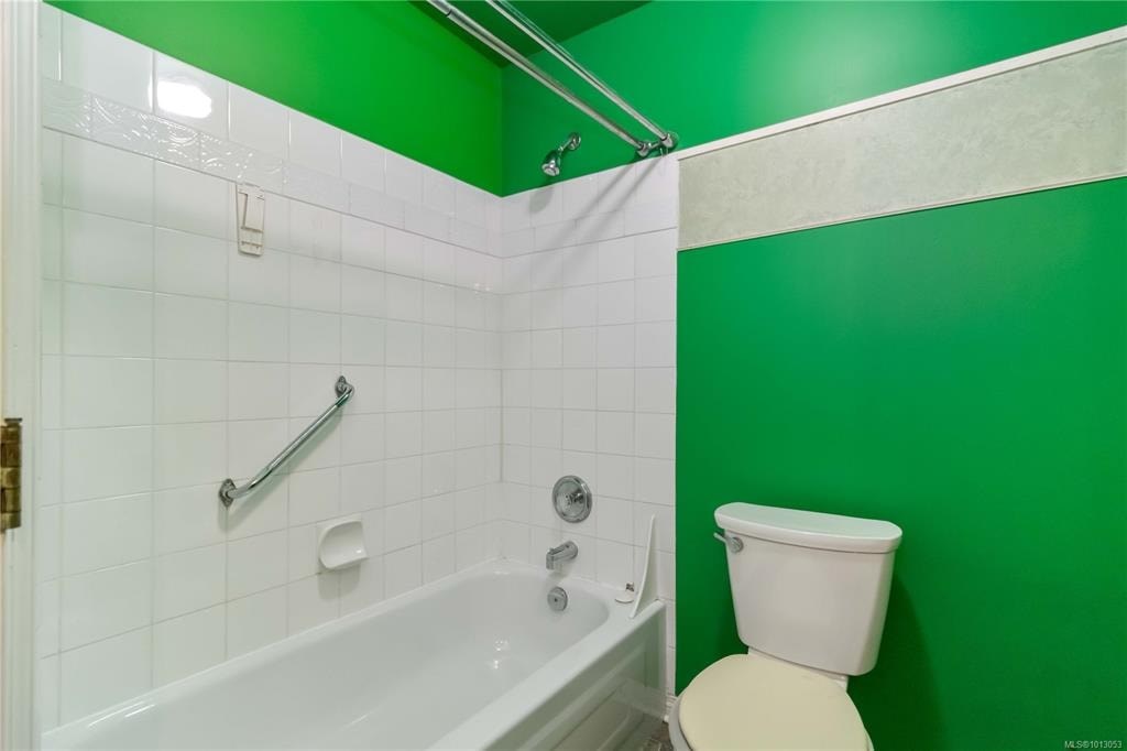 A white toilet sits next to a bathtub in a bathroom with green walls.