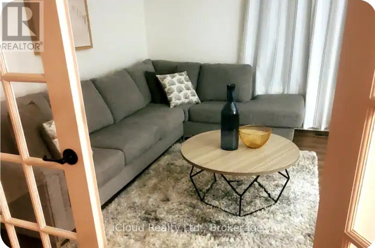 A grey couch with a pillow and a bottle on a wooden table.