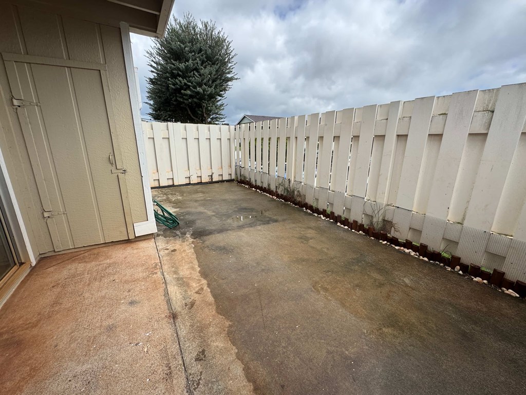 A concrete patio with a white fence and a green hose.