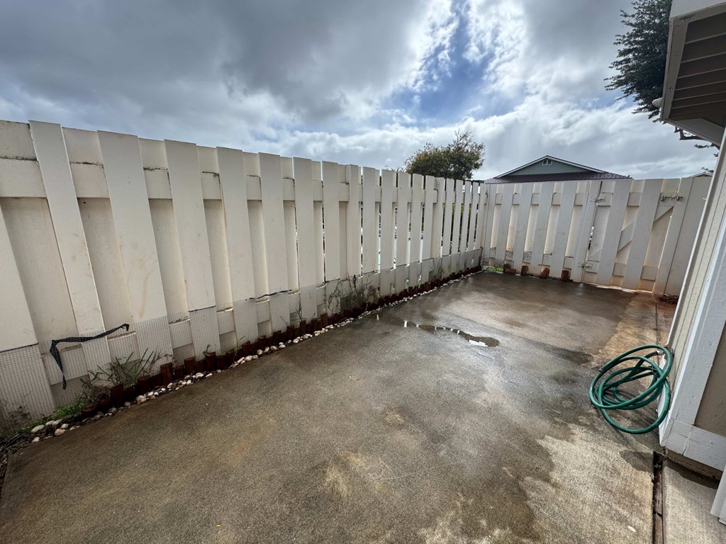 A concrete patio with a white fence and a green hose.