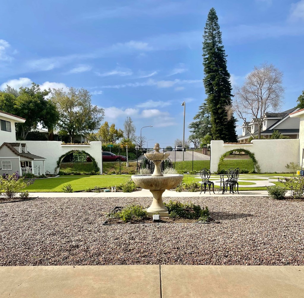 A garden with a fountain in the middle of a gravel area.