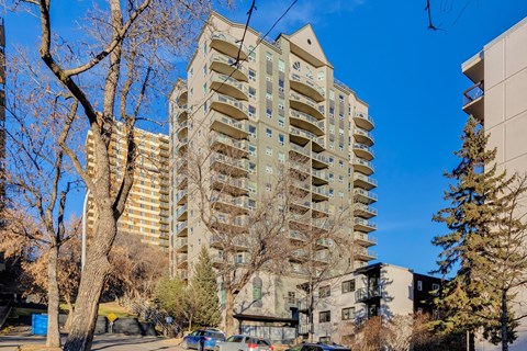A tall apartment building stands in the middle of a tree-lined street.