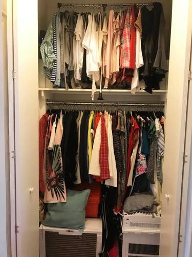 A white closet with clothes hanging on hangers.