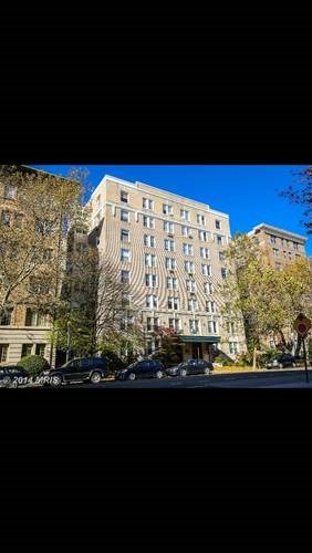A tall building with many windows is surrounded by trees.