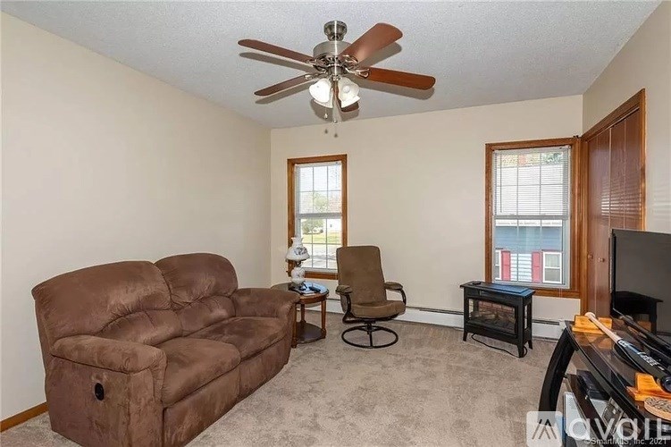 A living room with a brown leather couch, a fan, and a television.