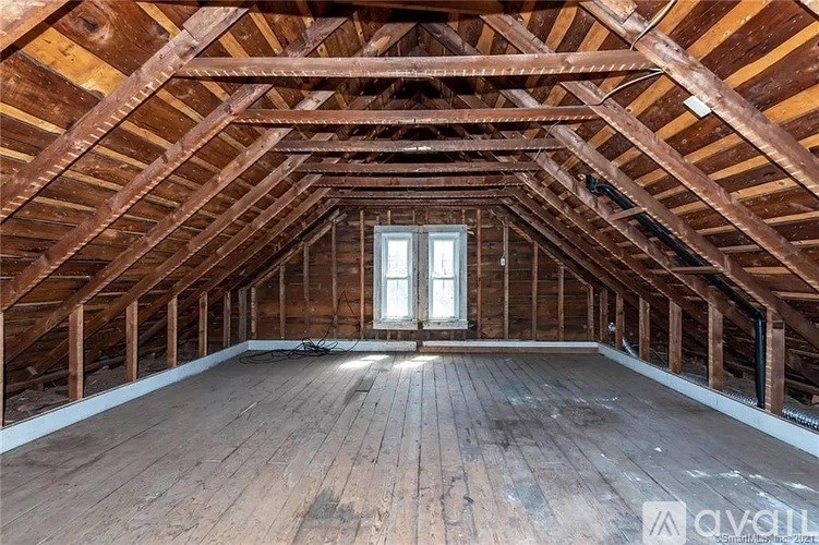A spacious attic room with wooden floors and exposed beams.