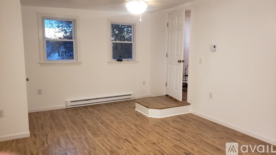 A room with wooden flooring and two windows.