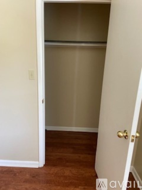 A white door with a gold handle is open to a room with a white wall and a brown floor.